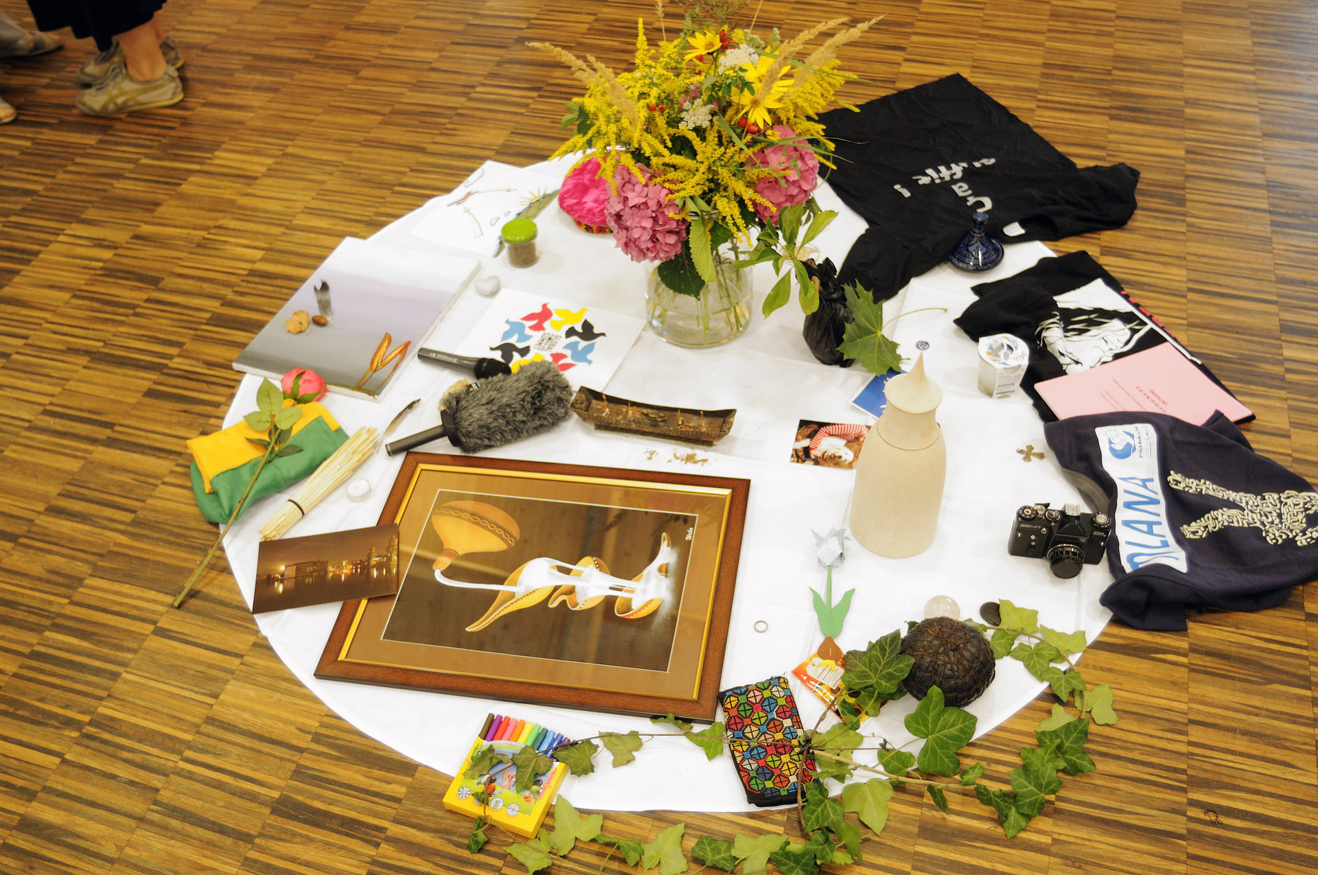 Global Peacebuilder Network - table set cloth on floor with several things on it. Flowers, a picture, plants, t-shirts